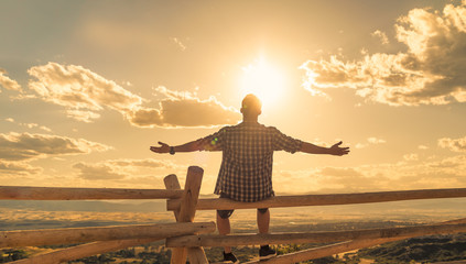 Happy man sitting outdoors looking up to the sky with arms outstretched. People freedom and...