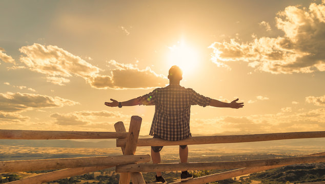 Happy man sitting outdoors looking up to the sky with arms outstretched. People freedom and happiness concept. 