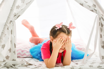 A little girl sits in a wigwam with pillows © Angelov