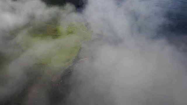 Rugged Faroe Islands coastline aerial reveal through sea clouds, high cinematic