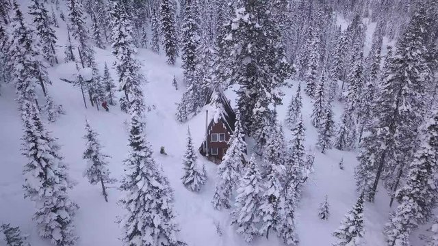 Skiers arriving at mountain cabin in the woods coverd in snow, Drone shot