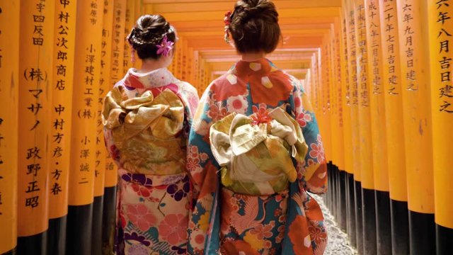 Geisha wearing kimono with flowers in hair walking through the Fushimi Inari-Taisha shrine in Japan