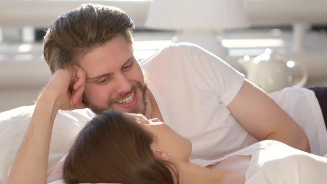 Happy family. Young love happy loving smiling married couple lying having fun together in bed, romantic scene in bedroom at home, Handsome man kissing beautiful woman. Valentine love. 4 K slow-motion
