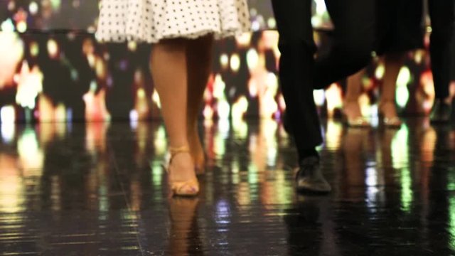 Couple's legs dancing a retro style music following the rhythm on vintage stage with other couples
