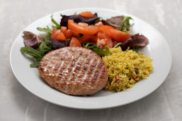 grilled hamburger with cereals and salad on white plate on ceramic background