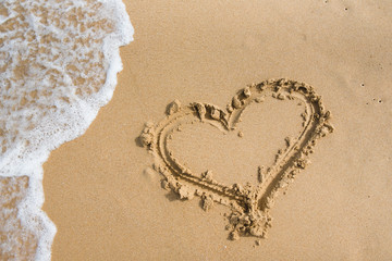 a heart drawn on the sand is washed away by a sea wave