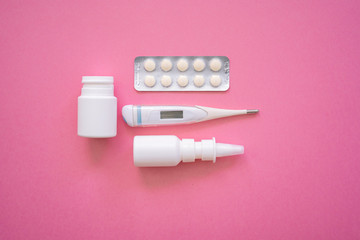 Blister tablets of vitamins pills, tablets, capsules, thermometer and nasal spray on pink background. Pharmacy drugstore and health theme. Selective focus. Virus and flu concept