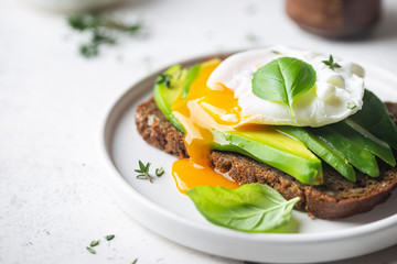 Healthy breakfast whole wheat toasted bread with avocado and poached egg over white background - obrazy, fototapety, plakaty