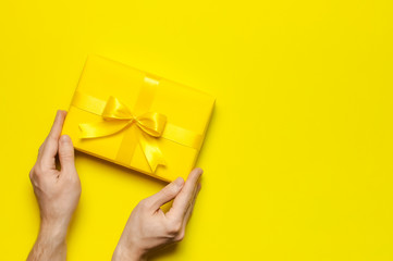 Male hands holding bright yellow gift present box with ribbon on yellow background top view. Flat...