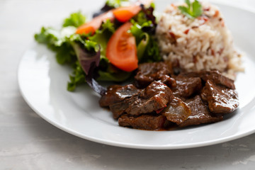 fried liver with salad and boiled rice on white plate