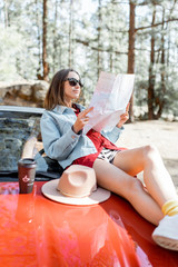 Young woman dressed casually traveling on a beautiful red cabriolet, sitting with map on the car...