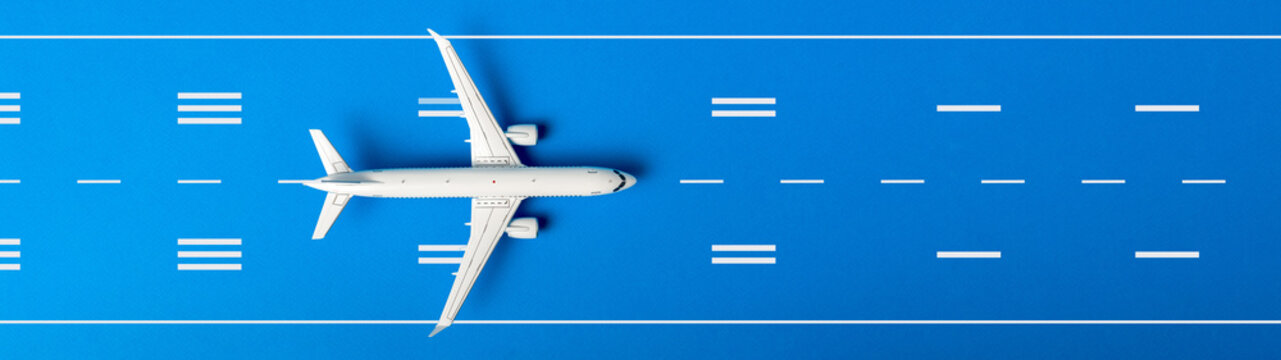 White plane, airplane on blue color runway background. Top view, flat lay. Summer travel, vacation concept. Banner