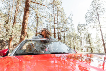 Young stylish woman enjoying traveling by convertible car on nature, looking out of the car in the...