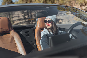 Portrait of a woman driving convertible car while traveling on the forest road, view through the...