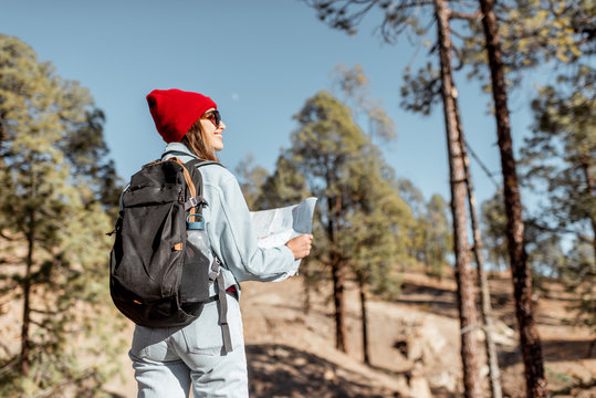 Young woman dressed casually walking with backpack in the forest highly in the mountains on the volcanic rocks