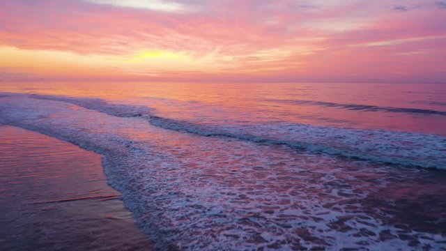 Spectacular pink purple sunset over ocean, waves breaking on beach. Low aerial