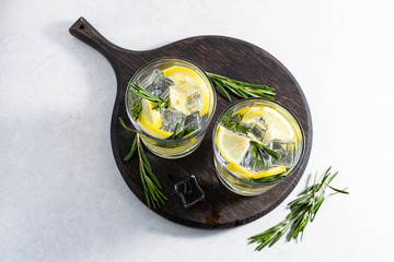 Two glasses of iced detox drink with lemon and rosemary on white marble table top view. Non alcoholic refreshing drink on the table.