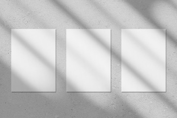 Three empty white vertical rectangle poster or business card mockups with diagonal window shadow on...