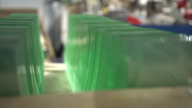 Focusing through a pile of clear glass panels on the shelf. Stack of glass sheets cut to size in a glass factory. Selective focus on sheets of green tempered clear glass. 