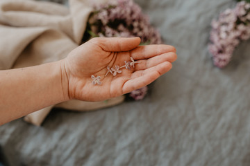 Close-up of hand holding purple lilac flowers with branch in bloom on blue linen sheet with neutral linen towel in the background, eco lifestyle concept, still life, vintage style with grain