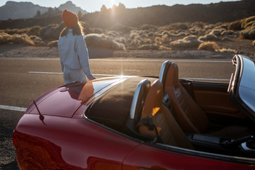 Woman enjoying beautiful rocky landscapes while standing with a car on the desert roadside during a...