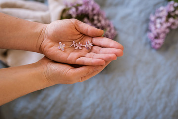 Close-up of hands holding purple lilac flowers with branch in bloom on blue linen sheet with neutral linen towel in the background, eco lifestyle concept, still life