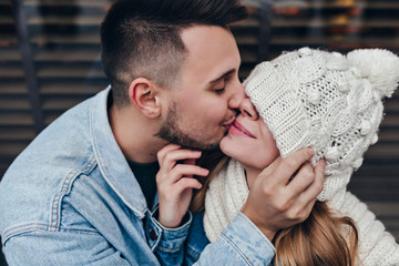 Dark-haired guy in denim jacket kissing his girlfriend. Caucasian man expressing love to funny...