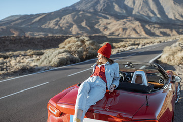 Woman enjoying beautiful rocky landscapes, sitting on the car hood on the roadside during a sunset....