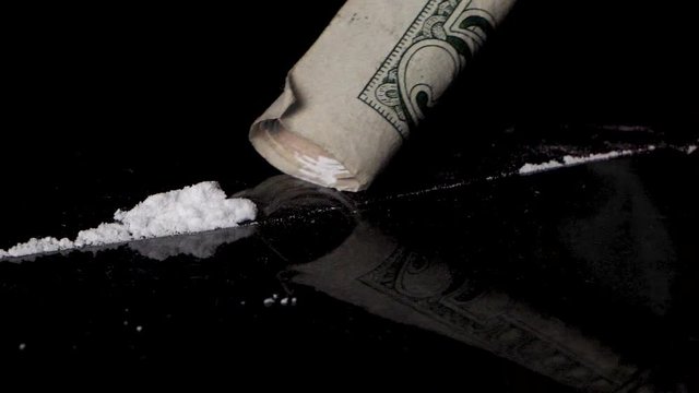 Snorting cocaine line with a rolled banknote, isolated on black reflective background. Close up, macro.