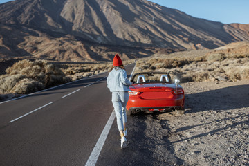 Young woman enjoying road trip on a sunset, running to the car on the roadside of the beautiful...