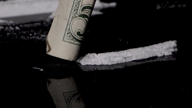 Snorting cocaine line with a rolled banknote, isolated on smooth black background. Close up, macro. Slow motion.