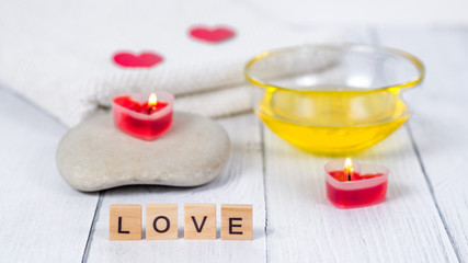 The concept of a Spa on Valentine's Day. Burn red heart-shaped candles, stones, massage oil, word love and white towel on a wooden background. Relaxation and wellness care. Bath procedure, cosmetology