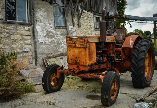 Rusty old tractor in field beside old rustic barn