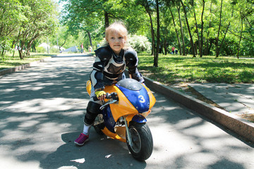 Little girl biker in motorcycle protection on a children's electric motorcycle rides a bike through the park at a biker festival motorcycle on an electric motor without emitting green technologies in