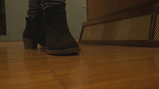 Tight close-up shot of a young woman waiting in short heal boots tapping foot impatiently at work.  Woman taps foot to music. 