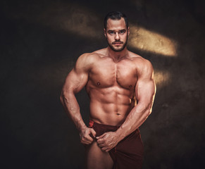 Obraz na płótnie Canvas Pensive muscular bodybuilder is demonstrating his leg muscles at dark photo studio.