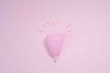 Pink menstrual cup with flower petals on a pastel pink background. The concept of the naturalness of menstruation and eco friendly