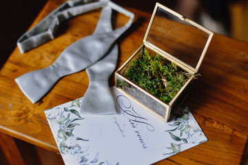 Untied bowtie and wedding rings in box and wedding invitations on the wooden table