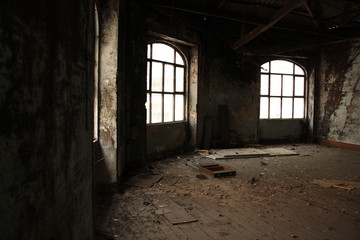 Interior of a large abandoned old dirty room with broken furniture, dirt and debris on the wooden floor.
