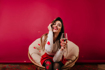 Excited long-haired woman having fun in valentine's day. Positive lady in white sweater siting on claret background with glass of water.