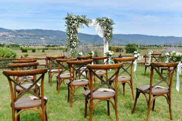 Fototapeta na wymiar Brown chiavari chairs and the decorated wedding archway with white flowers and greenery on the sunny day