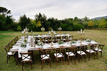 Top view of decorated with minimal floral bouquets and candles wedding celebration table with chiavari seats outdoors in the gardens