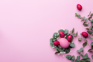 Bright burgundy quail eggs in eucalyptus twigs and gypsophila flowers on a pink paper background. Easter holiday concept. Copy space