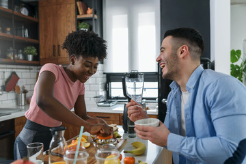 Young smiling interracial couple preparing healthy breakfast at home with lots of fruits. Healthy lifestyle.