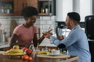 Obraz na płótnie Canvas Young smiling interracial couple preparing healthy breakfast at home with lots of fruits. Healthy lifestyle.