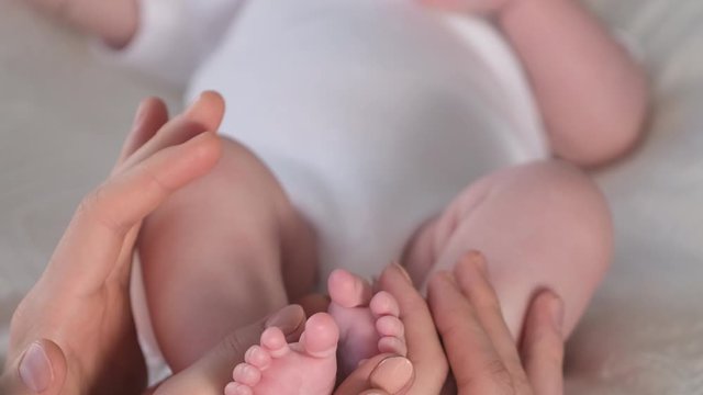 Happy Family. Mother and father holding feet legs of newborn baby child kid. Baby feet in parents hands. Baby's feet foot on female male hands, Close-up Maternity Parenthood Motherhood 4 K slow-motion