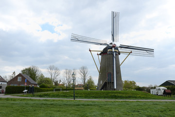 Fototapeta premium Traditional Dutch windmill standing in a green field with nearby houses, representing iconic rural landscape of the Netherlands.