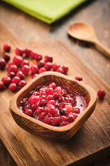 Cranberry jam in a wooden bowl on a wooden background.