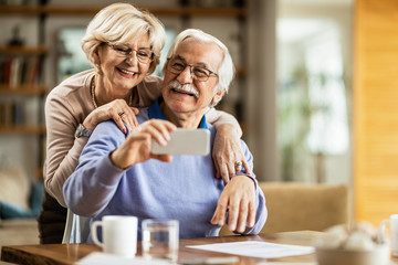 Happy senior couple having fun while taking selfie at home.