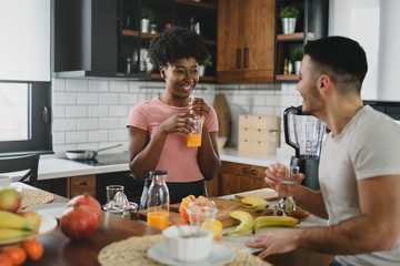 Young smiling interracial couple preparing healthy breakfast at home with lots of fruits. Healthy...